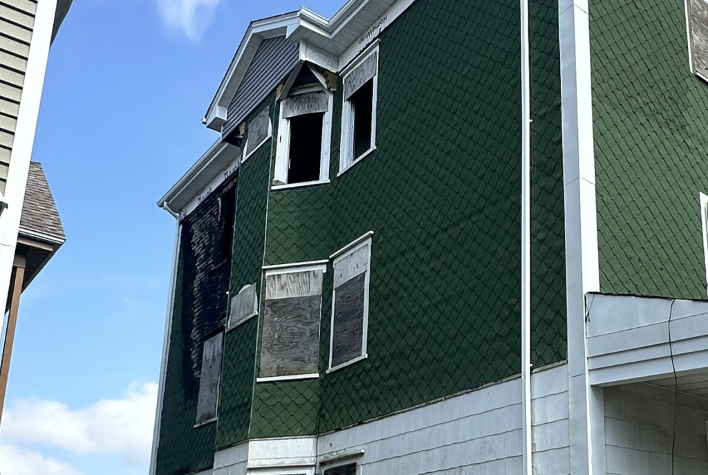 Green shingled house with boarded windows in southeastern Massachusetts